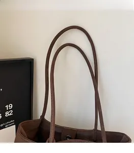 Detail of the dark brown leather tote bag showing slim shoulder straps and fine stitching