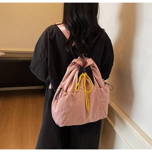 Rear view of a minimalist pink drawstring backpack worn by a model in a home setting