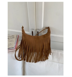 Detailed close-up of brown suede moon bag with bohemian fringe on a white sofa