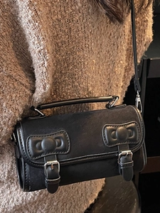 Minimalist black leather Boston bag with bow accents worn as a crossbody shoulder bag