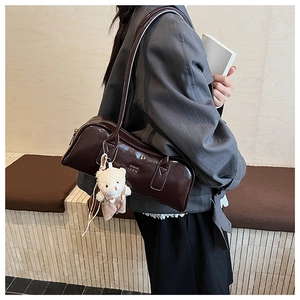 Detail of glossy brown Boston bag with metal logo and cute plush bear accessory