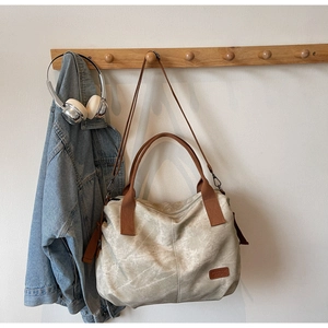 Close-up of distressed beige tote bag with brown handles and leather brand logo patch