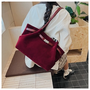 Detail view of burgundy suede tote bag with signature metal clasp and leather strap