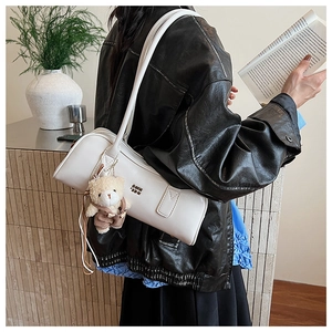 Detailed side view of white Boston bag with cute teddy bear charm on model shoulder