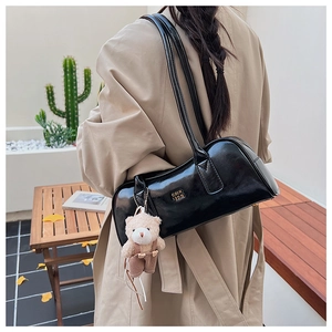 Detail of black glossy Boston bag with plush bear charm and metallic logo on woman's shoulder