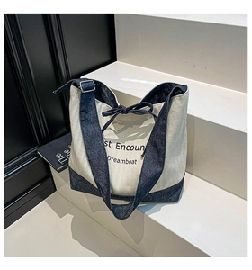 Close-up of beige herringbone canvas tote bag with navy denim straps and metal buckles