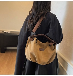 Detailed view of brown canvas messenger bag with wide strap on model in a room
