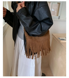 Detailed view of brown suede shoulder bag featuring long bohemian tassels on a female model