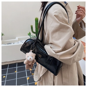 Detail of black patent leather Boston bag with a teddy bear charm on a trench coat model