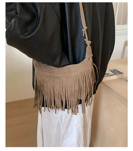 Detail of a brown suede half-moon bag featuring long fringes and adjustable strap