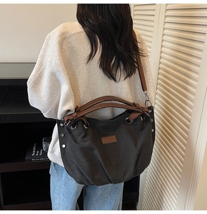 Detail of black canvas tote bag with brown leather handles and adjustable shoulder strap