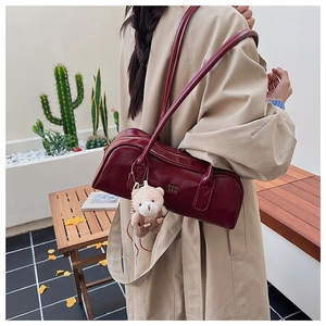 Detail view of burgundy leather Boston bag with plush bear charm on minimalist shoulder strap