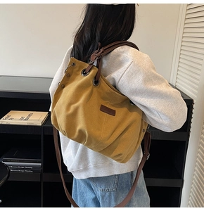 Close-up of a mustard yellow canvas tote bag with brown leather handles and metal eyelets