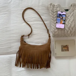 Detail shot of brown suede crossbody bag with long tassels on a textured beige fabric