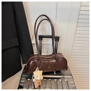 Detail of a coffee brown leather Boston bag with a bear charm on a silver suitcase