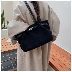 Close-up of minimalist black suede bucket bag with metal buckle and long shoulder strap