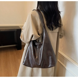 Detail view of deep brown oily leather tote bag with vintage texture on person wearing trench coat
