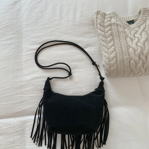 Close-up of black suede moon bag featuring long tassels and knotted rope strap