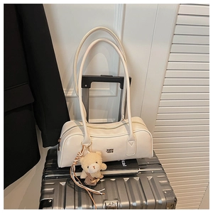 Chic beige Boston bag with plush bear charm displayed on a metallic travel suitcase