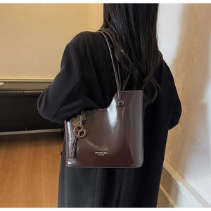 Detail of a dark brown glossy tote bag with asymmetrical curved opening and knotted charm
