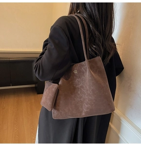 Macro shot of brown suede tote bag featuring metallic brand logo and hanging mini pouch detail