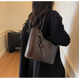Detail of dark brown glossy tote bag with heart charm and woven strap on model shoulder