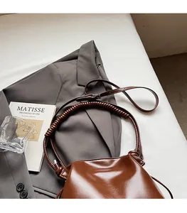 Detail of a brown glossy bucket bag featuring unique spiral wrapped handles and smooth leather