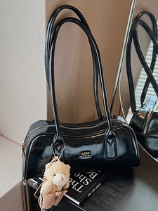 Minimalist black patent leather Boston bag with long straps and bear pendant