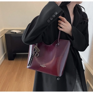 Detail of high-gloss burgundy tote bag with luxury charm and brand logo on black blazer