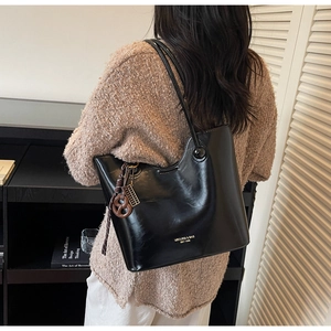 Close-up of black glossy tote bag with gold brand logo and brown twist pendant charm