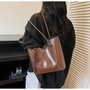 Detailed view of brown leather tote bag with elegant side woven pendant and brand lettering