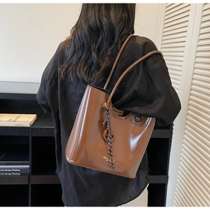 Detailed shot of a brown glossy tote bag featuring unique woven rope charms on the shoulder strap