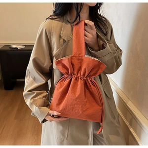 Dettaglio della borsa in tela arancione con coulisse, texture a pieghe ed etichetta nera