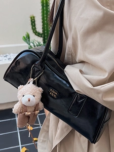 Glossy black Boston bag with gold logo and plush bear charm on a trench coat