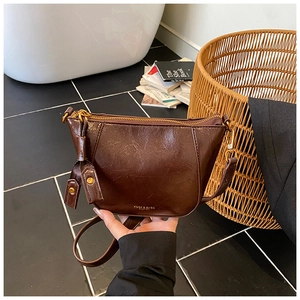 Detail of a brown crescent shoulder bag featuring a gold zipper and brand logo text