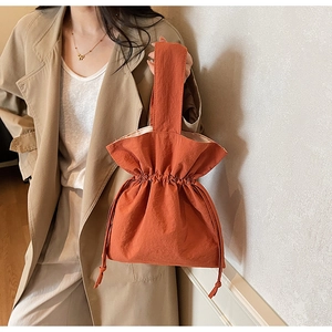 Dettaglio di una borsa a secchiello arancione con coulisse, trama a pieghe e manico largo