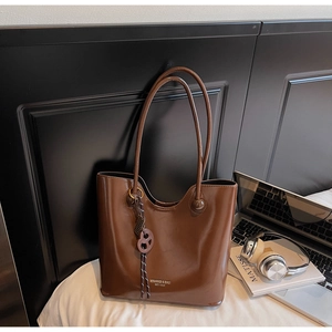 Detail of glossy brown patent leather tote with a stylish cookie-shaped charm on white bed