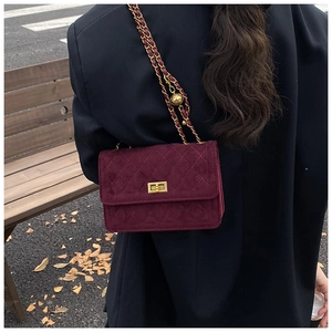 Detail of burgundy quilted suede handbag with gold ball chain strap and turn-lock closure