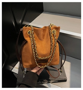 Détail d'un sac seau en daim marron avec cordon de serrage et chaîne dorée