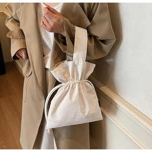 Dettaglio della borsa a secchiello beige minimalista con texture a pieghe in mano