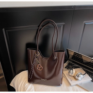 Close-up of dark brown glossy tote bag with pretzel charm and minimalist texture