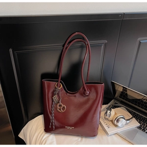 Detail of dark burgundy patent leather tote bag with unique pretzel charm and gold logo