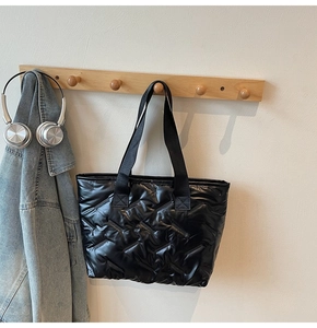 Close-up of black quilted puffer tote bag with diagonal stitching on a wooden hook