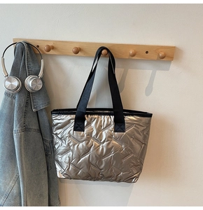 Detail of metallic quilted tote bag texture with wide black strap on wooden hook
