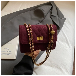 Close-up of wine red quilted suede bag with golden sphere chain and metal turn lock