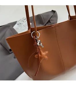 Detail of caramel leather tote bag handle with star charm and metallic key pendant