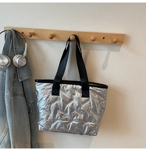 Quilted metallic silver tote bag with black straps hanging on wooden wall hooks