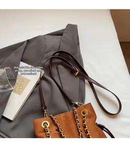 Détail de la bandoulière réglable d'un sac seau en daim marron avec chaîne dorée