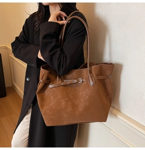 Brown matte leather tote bag with decorative buckle shown on shoulder of a model