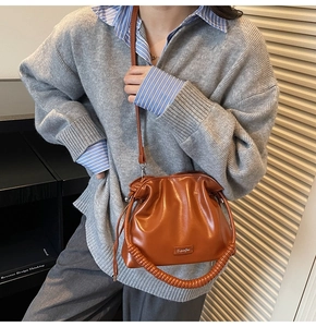 Brown pleated bucket bag with twisted handle shown on model in a casual home setting